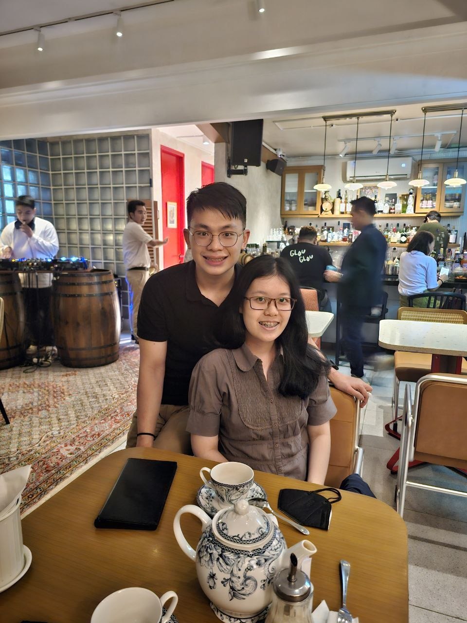 Rey and Feli posing together at a restaurant table with a teapot in the foreground