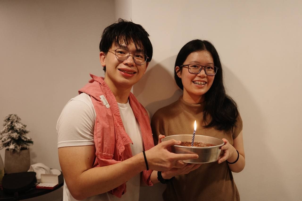 Rey and Feli smiling together while holding a birthday cake with a candle