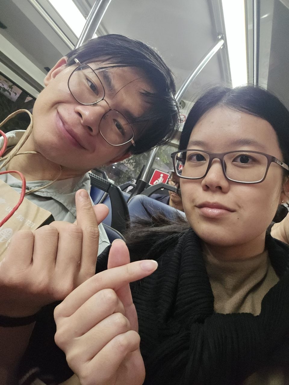 Rey and Feli taking a selfie on a bus while making finger hearts